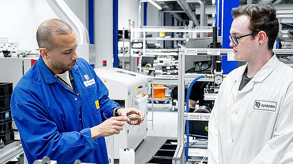 A person in a blue coat and a person in a white coat on the production floor