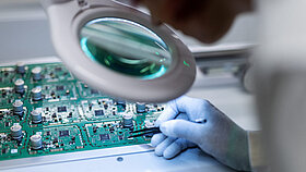 Person schaut durch Lupe auf ein Embedded Modul