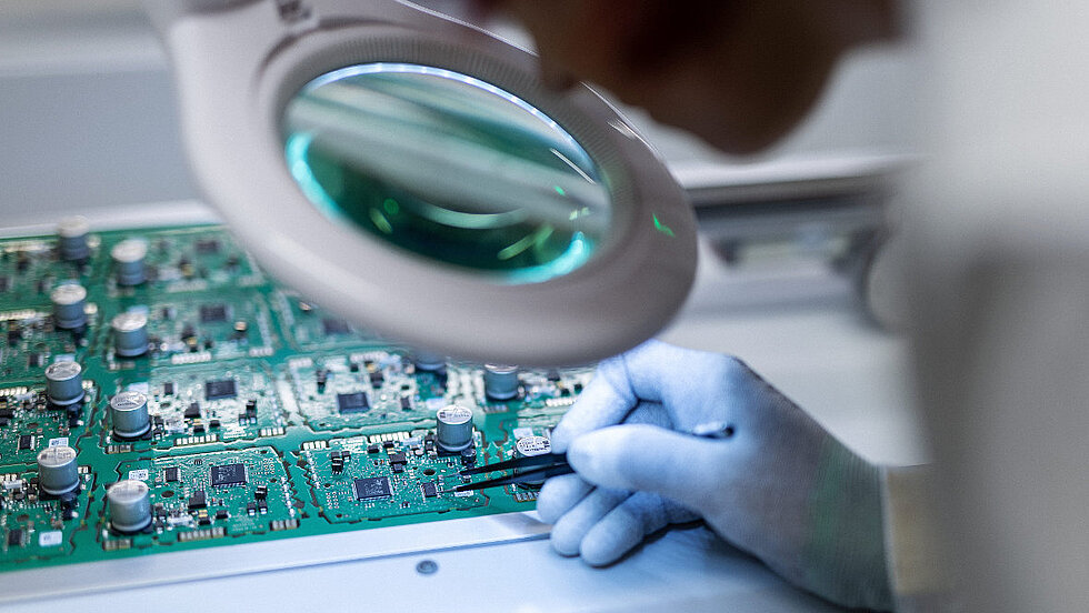 Person schaut durch Lupe auf ein Embedded Modul