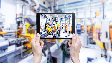 Hände halten ein Tablet in der Hand vor einer Produktionslinie