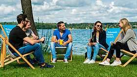 Junge Erwachsene sitzen in Liegestühlen am See