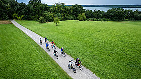 Eine Gruppe Fahrradfahrer auf einem Feldweg zwischen grünen Wiesen