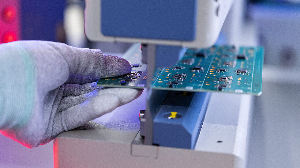 Eine Hand mit Handschuh hält ein Embedded Modul beim Nutzentrennen