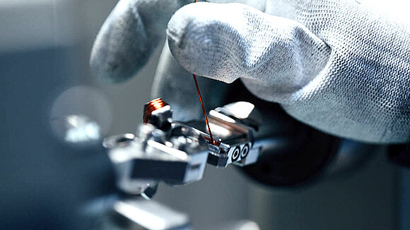 A gloved hand holds a copper wire while winding it for a torque motor