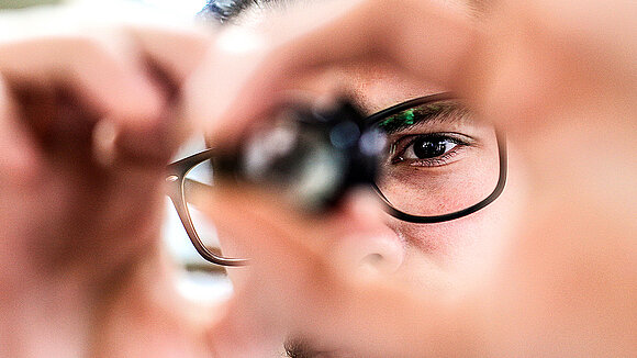 A person with glasses looks through a small magnifying glass