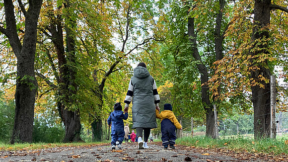 Eine Frau von hinten mit 2 Kindern an der Hand im Park