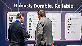 Two people seen from behind, standing in front of an exhibition booth