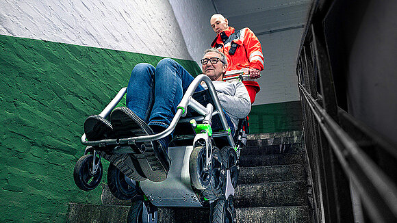 A paramedic is transporting a person up a flight of stairs using a stairlift