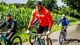 Oliver Zeidler auf einem E-Mountainbike im Hintergrund ein Maisfeld und andere Radfahrer