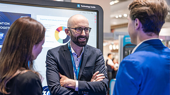 Ein TQ Mitarbeiter erklärt etwas an einem großen Monitor auf einer Messe