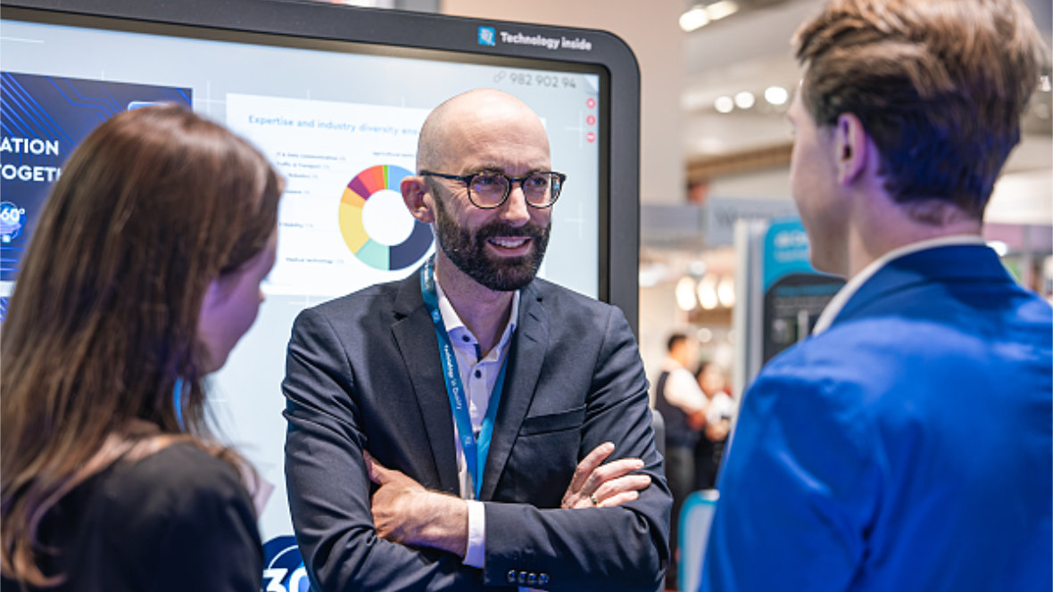 Ein TQ Mitarbeiter erklärt etwas an einem großen Monitor auf einer Messe