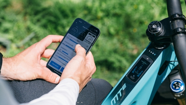 Eine Person hält ein Smartphone in der Hand und sitzt auf einem E-Bike