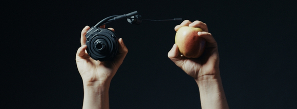 One hand is holding up a TQ HPR motor, and the other hand is holding up an apple for comparison