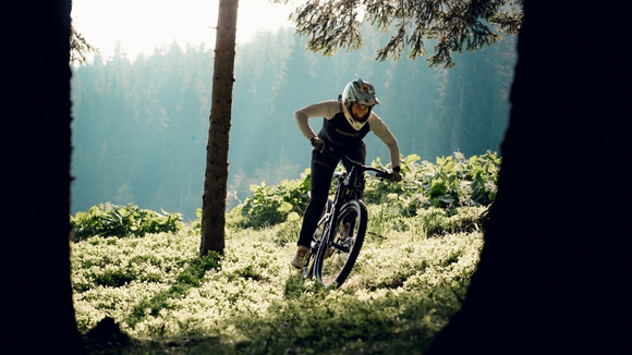 Eine Mountainbikerin im Wald zwischen Bäumen