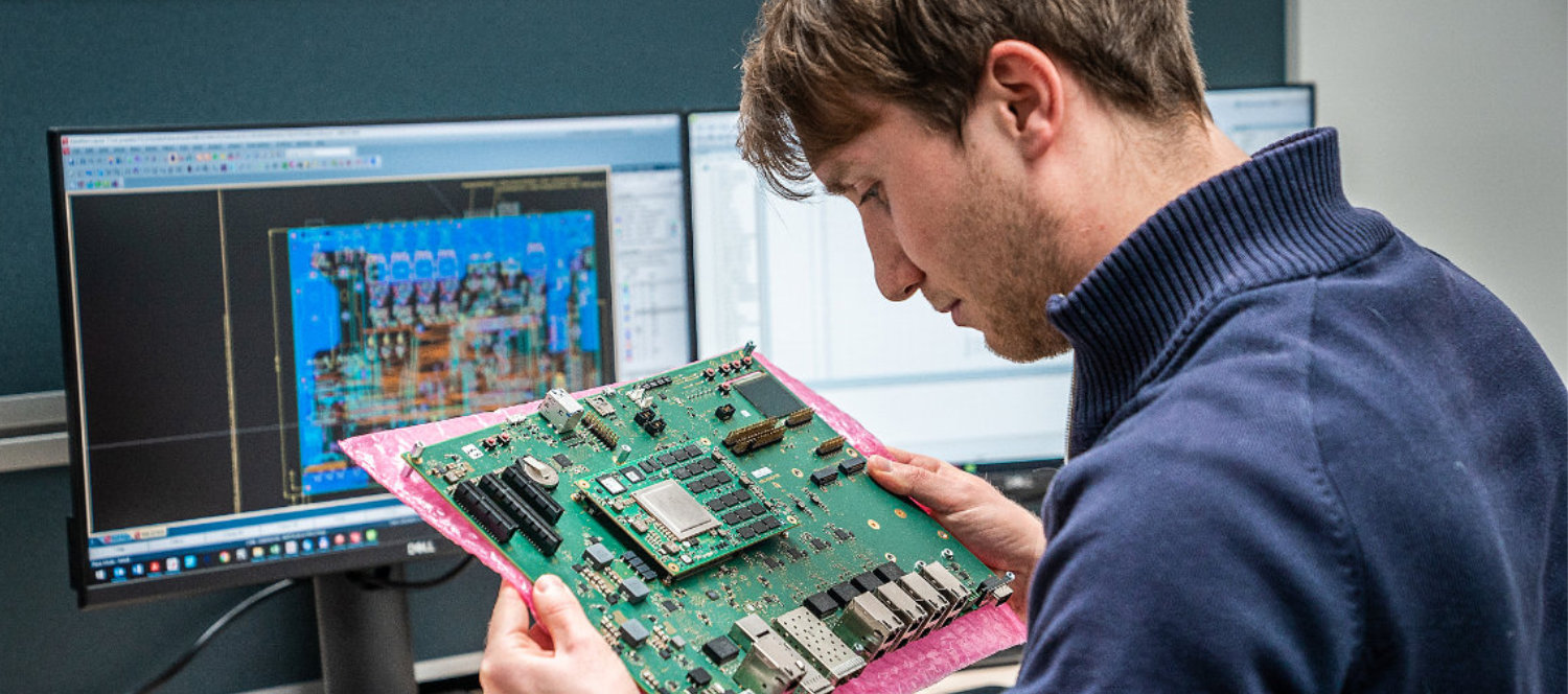 Mann mit einem Embedded Modul in der Hand vor einem Bildschirm