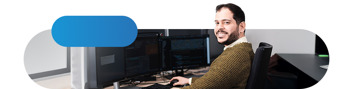 A man sits in front of a PC screen and looks into the camera