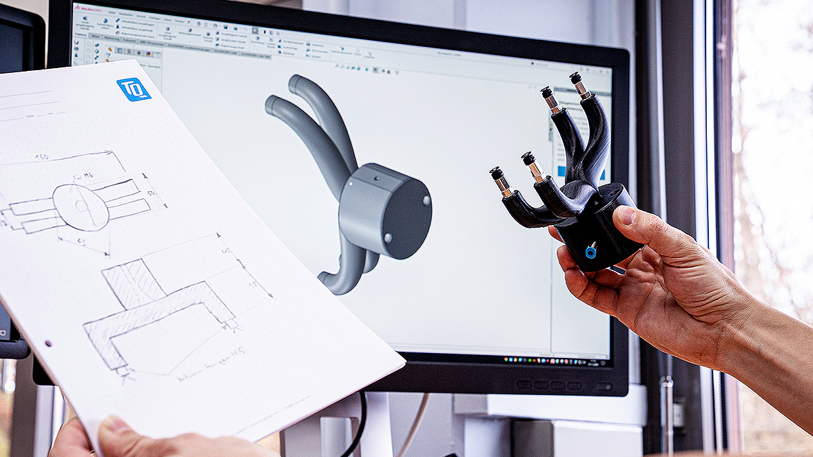 A sketch and a component in the hands of a person in front of a PC screen