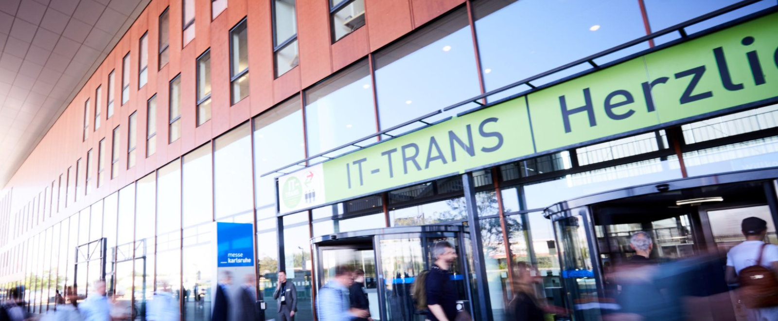 Eingang der IT Trans Messe mit leicht verschwommenen Personen vor dem Gebäude