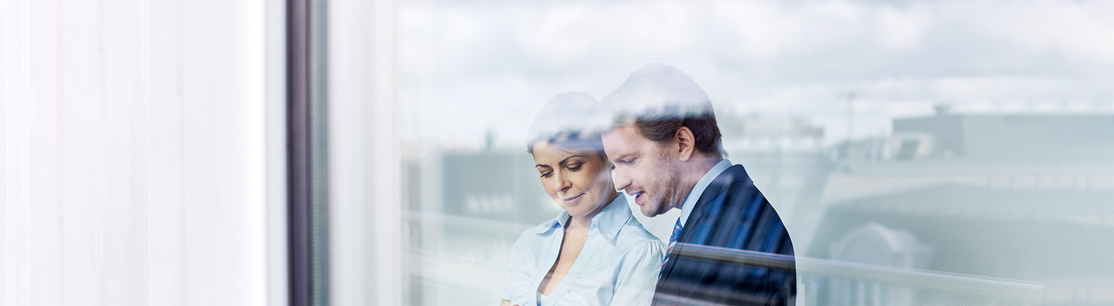 Two people holding a tablet computer behind a plate of glass